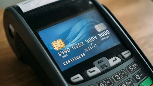 Mão inserindo cartão de crédito em maquininha de pagamento numa loja no exterior