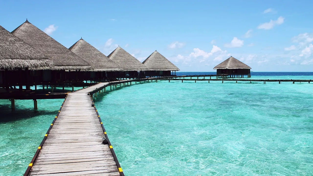 Bangalôs sobre a água em resort tropical com piscina e mar azul-turquesa