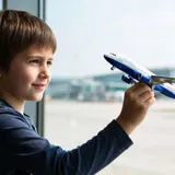 Criança segurando um avião de brinquedo diante da janela de um aeroporto