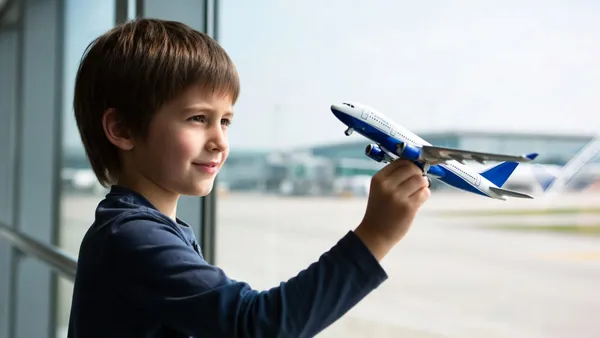 Criança segurando um avião de brinquedo diante da janela de um aeroporto