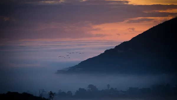 Vista aérea de cidade litorânea com montanha ao fundo ao entardecer